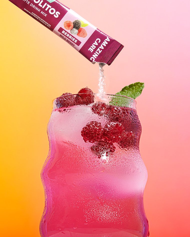 Sobre de electrolitos sabor berries vertiéndose en un vaso con frambuesas