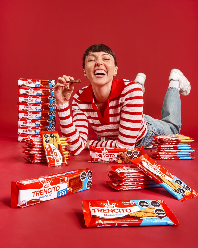 Mujer riendo rodeada de chocolates Trencito sobre fondo rojo